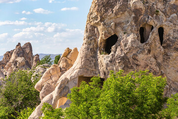 Landscape of Cappadocia featuring rock formations with cave openings and lush greenery under a...