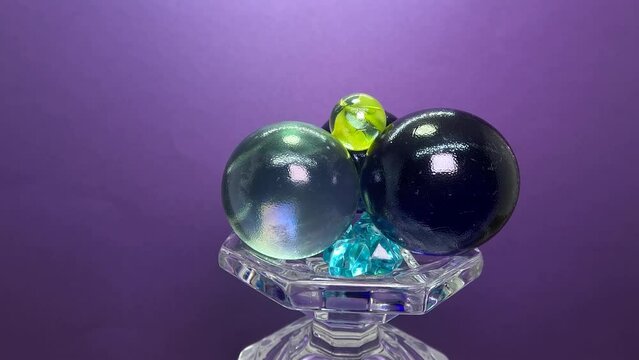 Glass balls with blue diamond-shape fake crystals on a glass display rotating on a purple background