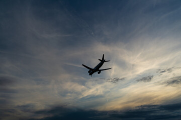 Silhouette of an airplane against the cloudy sky in the fading evening light