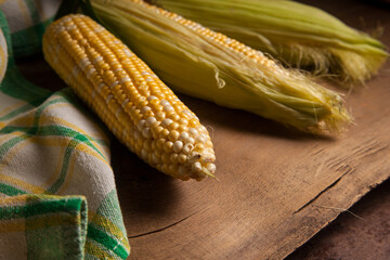 Close up view of three cobs sweet corn with green leaves on wooden background..