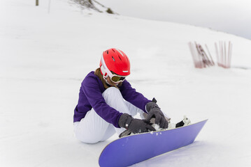 Girl Closing the Stratches of her Snowboard Binding, Sitting in the Snow