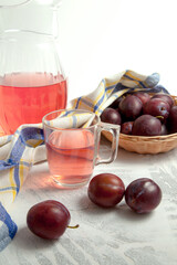 Plum Compote in jug with purple plums on white wooden background. .