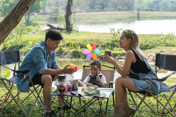 Obraz premium Young Asian family with father mother and son sitting on camping chair in camp site