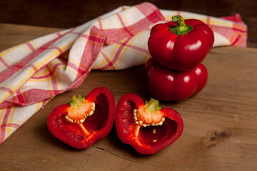 Two whole and halves of red bell pepper on wooden background with red kitchen towel. .