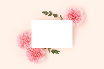 Empty paper card mockup, pink carnation flowers and green eucalyptus branches on a beige background. Cute festive concept.