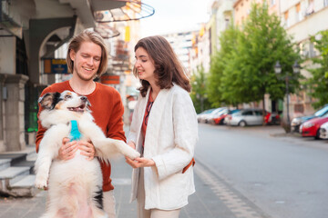 Happy young couple, man and woman hugs their dog Aussie at the street. Family walking together in city with pet