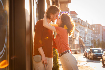 Side view of Young couple Caucasian man and woman, are kissing on street. Sunset light city in...