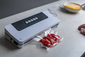  Sealing machine vacuum packing with plastic bag of red pepper at white table, closeup