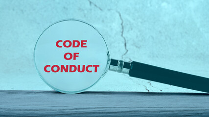 Business concept text. The words CODE OF CONDUCT through a magnifying glass on an abstract...