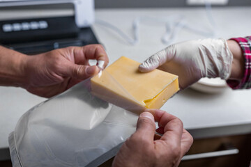 Close-up of men's hands sealing cheese into an airtight bag using a vacuum sealer