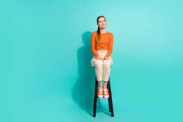 Full size photo of pleasant girl dressed orange shirt sitting on stool look at discount empty space...