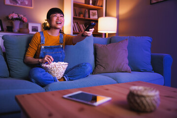 Woman turning on TV using remote control relaxing at home late at night