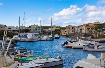 Vista del puerto de Stintino en Cerdeña, Italia, durante la primavera. La imagen muestra una variedad de barcos y yates atracados en el puerto, rodeados de edificios mediterráneos. 