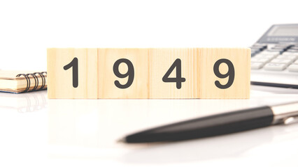 The numbers 1949 written on wooden cubes in a composition with a calculator, a pen on a white...