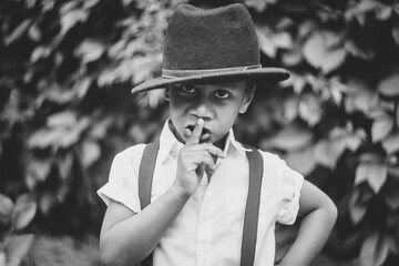 close-up of a boy in a 20s style hat seriously holding his finger to his mouth as a sign of silence