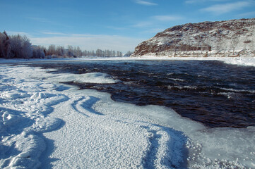 A frozen river bank with a distant mountain under a cloudy sky