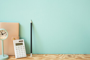 Workspace diary note, calculator, pencil, clock on wooden desk. mint wall background