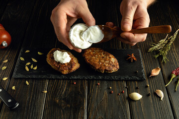 Cooking a delicious breakfast of cutlets and sour cream on the kitchen table with the hands of a...