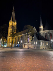 Historic church lit up at night with surrounding trees and cobblestone plaza. Perfect for themes of...