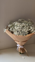 Elegant bouquet of white baby's breath flowers wrapped in brown paper with a white ribbon, placed...