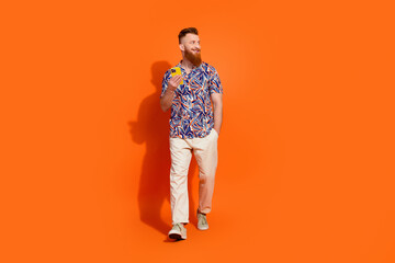 Fototapeta premium Full length photo of positive dreamy guy dressed print shirt typing device looking empty space isolated orange color background