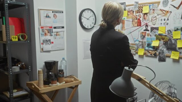 A thoughtful woman detective stands in an office analyzing a crime investigation board with photos and notes.