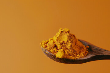 Close-up of vibrant turmeric powder heaped on a rustic wooden spoon against a warm, monochromatic orange background