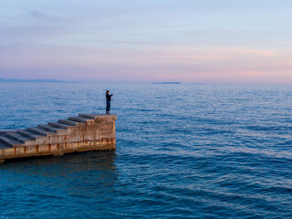 Naklejka premium Girl on a Pier Overlooking the Sea - Pink Sunset Sky