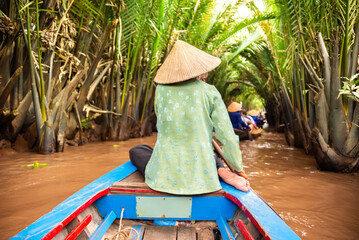 Woman with asian hat rowing in a boat on jungle river