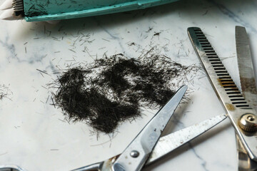 Scissors, thinning scissors and a comb are on a table with a pile of hair. The scene suggests that...
