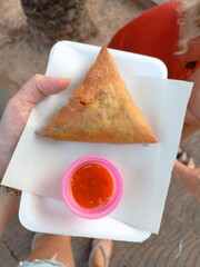 a woman holds a tray of food purchased at an Asian market. samosa with spicy sauce, street food....