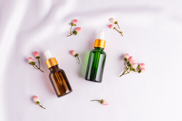 Two different bottles with a dropper with serum or a cosmetic natural face and body care product on white satin among decorative berries. Top view.