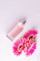 Elegant bottle of women's perfume with delicate fragrances on a white satin background with flowers pink gerberas. Empty packaging. presentation.