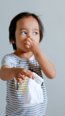 cute Asian child holding stinky tissue and covering his nose