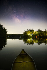 A yellow canoe on a calm lake at night below the Milky Way Galaxy. The stars are reflected on the...