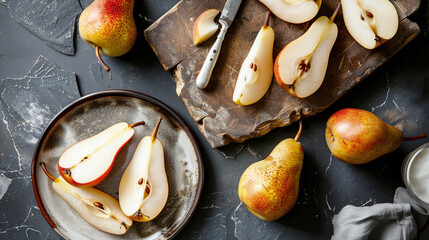 Top-down view of fresh pears, whole and sliced, arranged on a dark slate background with a rustic cutting board and knife. The setting emphasizes natural beauty and simplicity.
