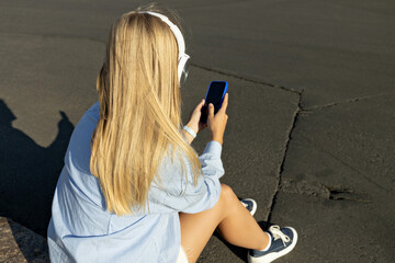 A girl in headphones and with a phone on the street.