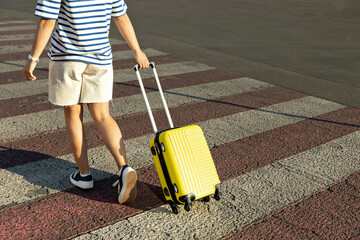 A girl, blonde, with a yellow suitcase on the street.