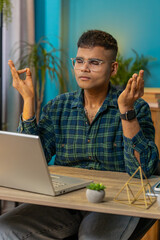 Indian man working on laptop, breathes deeply, eyes closed meditating with concentrated thoughts,...