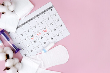 Women's menstrual pads, tampons, female menstruation calendar and alarm clock on a pink background.