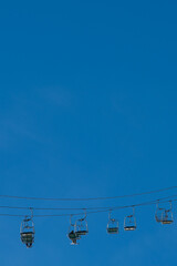 Lift chairs with skiers sitting in them ride along a cable from one support to another at the resort against the backdrop of a cloudless blue sky