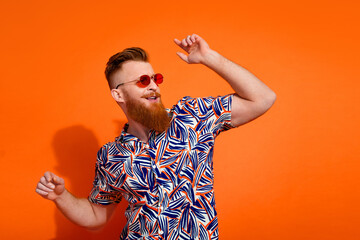Portrait of ecstatic brutal man wear print shirt in glasses dancing look at event promo empty space isolated on orange color background