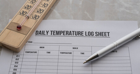 A daily temperature log sheet form on the desk . Thermometer and pen on the table