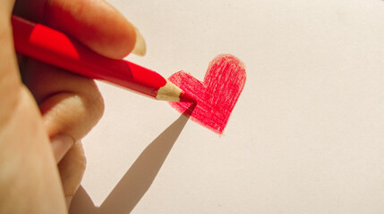 Hand drawn red heart on white paper close up in sun light as illustration of love and romantic relationship