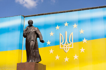 The statue of an outstanding Ukrainian figure Taras Shevchenko is located against the background of a bright Ukrainian flag. Bright sunny weather enhances the visual appeal of the scene.