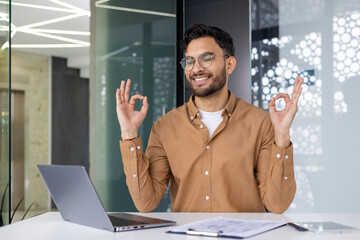 Young professional practicing yoga at work desk in modern office