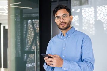 Confident young professional in blue shirt holding smartphone at modern office