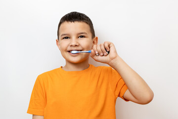 A little boy in an orange T-shirt carefully brushes his teeth.