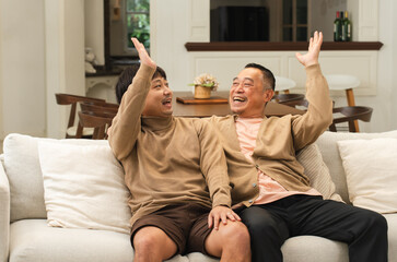 Cheerful Asian old man giving high five to happy middle aged son, celebrating good news. Smiling...