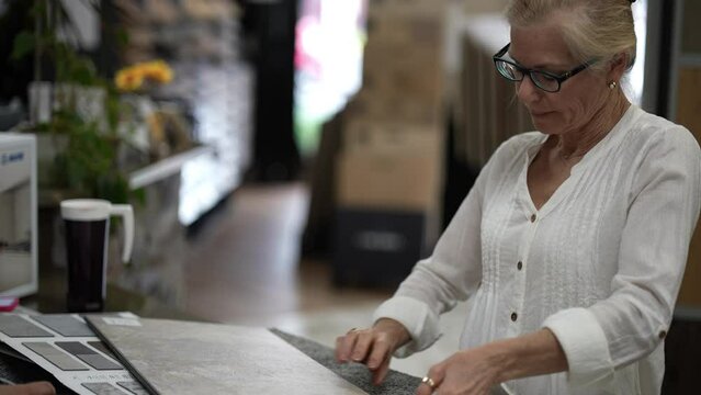 Happy mature woman looking at samples of floor tiles in a store, consider using vct or engineered tile in a home renovation project.